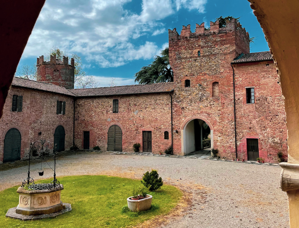 Panoramica degli interni del Castello di Castelnovo Val Tidone, nel Comune di Borgonovo Val Tidone. Al centro del cortile un piccolo spazio erboso con un antico pozzo. Il resto del cortile è coperto di ghiaia. Si può notare l'ingresso del castello con torre e una torre laterale sulla sinistra. Inoltre si può notare anche la struttura muraria in mattoni rossi.